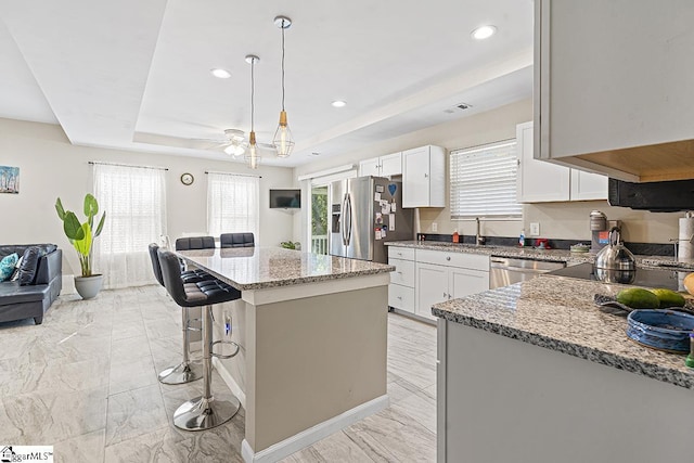 kitchen with stainless steel appliances, a raised ceiling, marble finish floor, light stone countertops, and a breakfast bar area