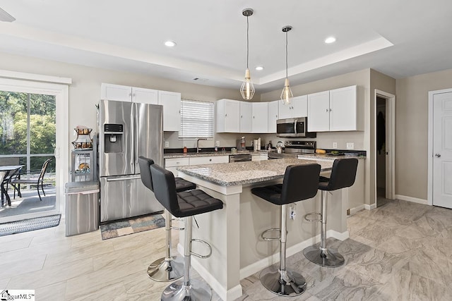 kitchen with white cabinets, a tray ceiling, baseboards, a kitchen bar, and appliances with stainless steel finishes