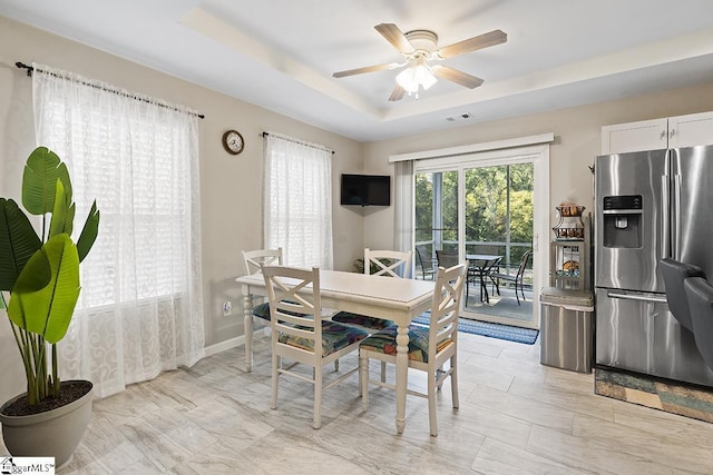 dining area with a tray ceiling, visible vents, a ceiling fan, and baseboards