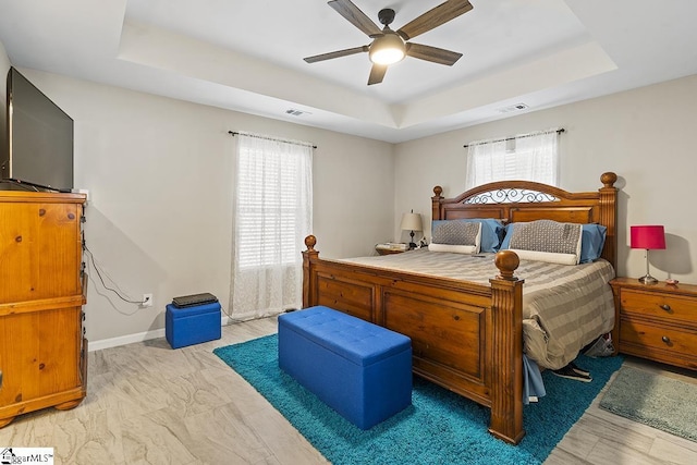 bedroom featuring ceiling fan, baseboards, visible vents, and a raised ceiling