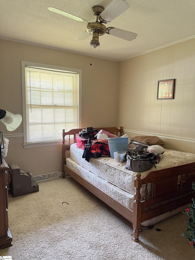 bedroom featuring a ceiling fan, ornamental molding, a decorative wall, a textured ceiling, and carpet flooring