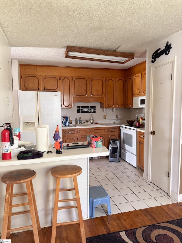 kitchen with brown cabinets, a kitchen bar, light countertops, and white appliances