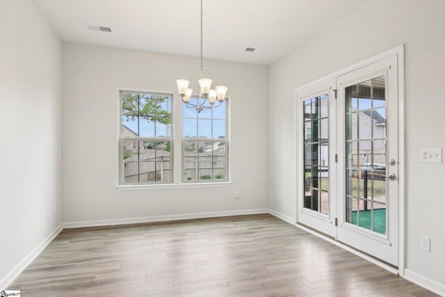 unfurnished dining area with a chandelier, visible vents, wood finished floors, and a wealth of natural light