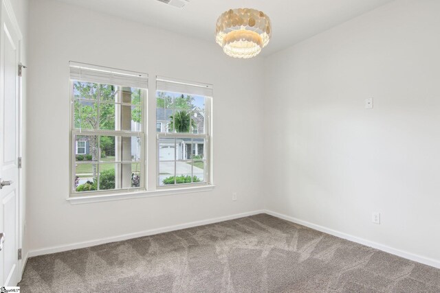 carpeted empty room with an inviting chandelier, visible vents, and baseboards