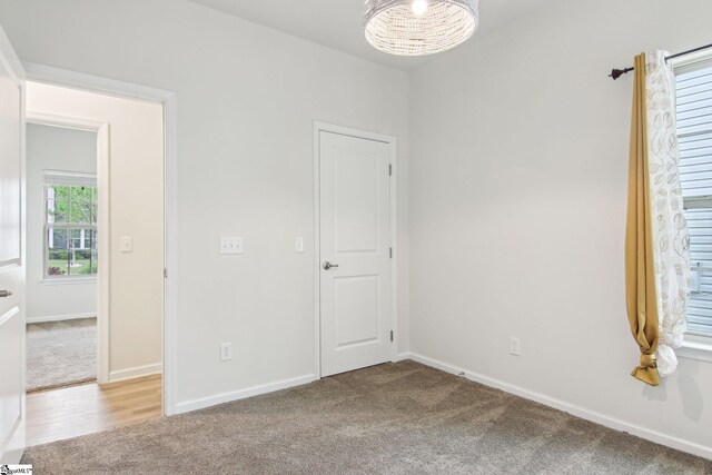 empty room with baseboards, a notable chandelier, and light colored carpet