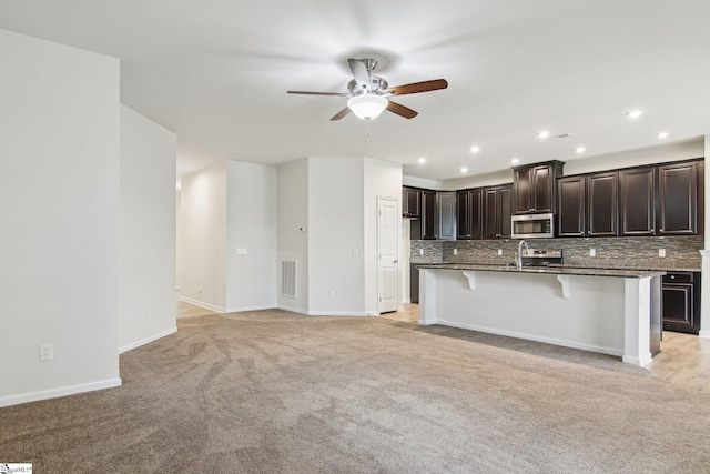 kitchen featuring stainless steel appliances, ceiling fan, a breakfast bar, visible vents, and light colored carpet