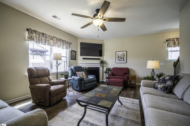 living room featuring wood finished floors, a ceiling fan, visible vents, and a fireplace