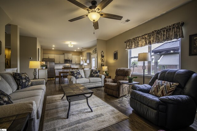 living area with dark wood-type flooring, visible vents, a wealth of natural light, and ceiling fan