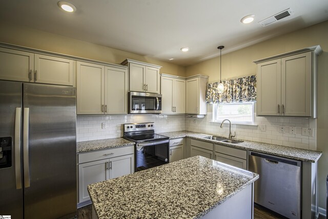 kitchen featuring light stone counters, a center island, a sink, stainless steel appliances, and visible vents