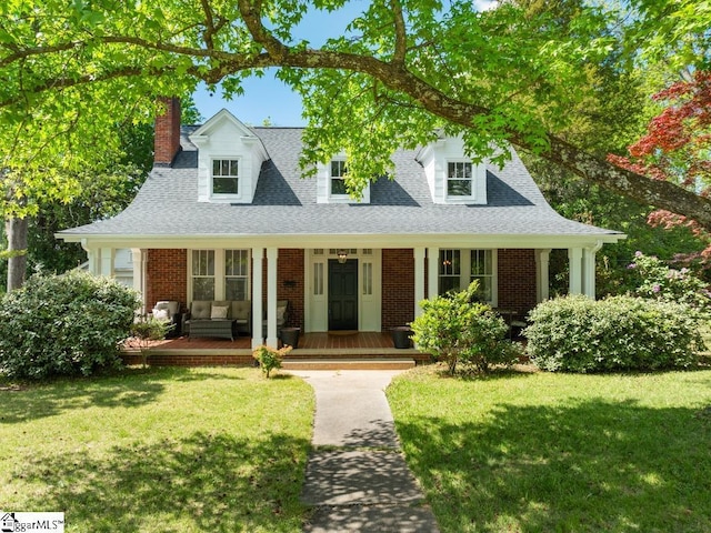 cape cod home featuring a chimney, a porch, a front yard, brick siding, and roof with shingles