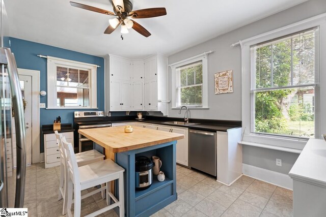 kitchen featuring white cabinets, stainless steel appliances, a sink, butcher block countertops, and ceiling fan