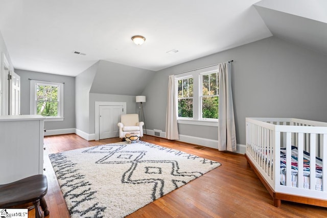 bedroom with baseboards, vaulted ceiling, visible vents, and hardwood / wood-style flooring
