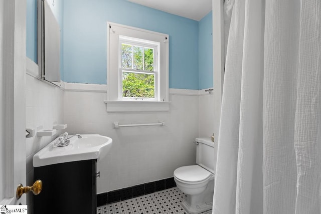 bathroom with tile walls, a wainscoted wall, vanity, and toilet