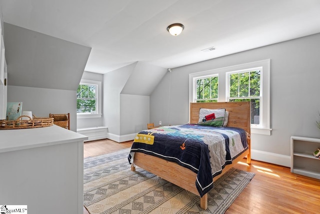 bedroom featuring light wood-type flooring, baseboards, visible vents, and lofted ceiling