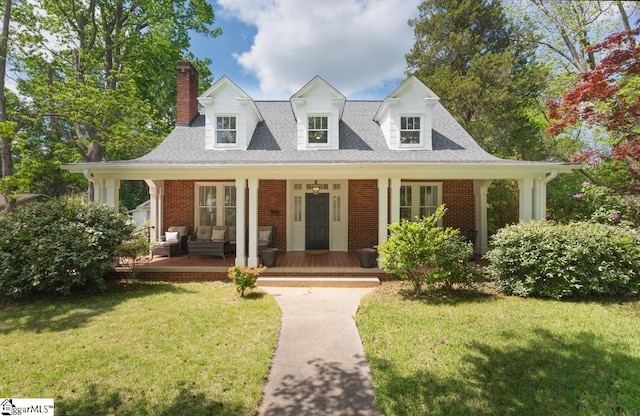 view of front of home with a front lawn, a chimney, covered porch, and brick siding