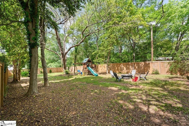 view of yard with a fenced backyard, a fire pit, and a playground