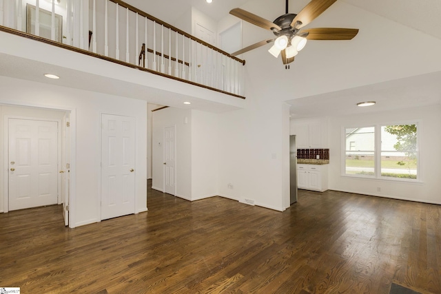 unfurnished living room featuring high vaulted ceiling, baseboards, a ceiling fan, and dark wood-type flooring