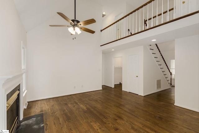 unfurnished living room with wood finished floors, a ceiling fan, a towering ceiling, and stairway