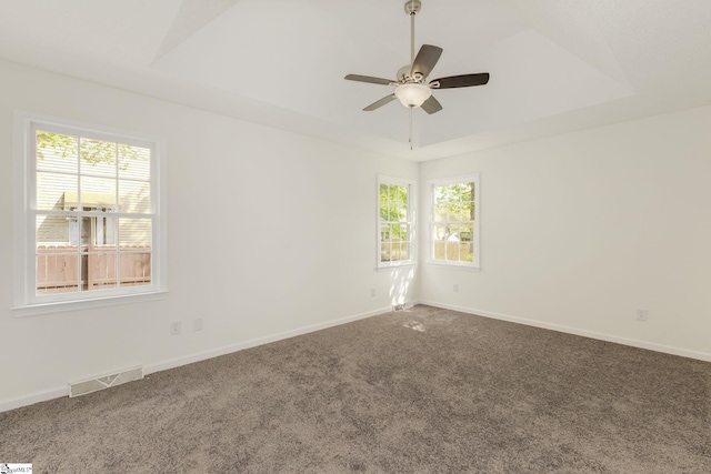 carpeted empty room featuring visible vents, a raised ceiling, ceiling fan, and a healthy amount of sunlight