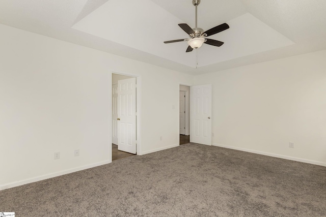 empty room featuring dark carpet, baseboards, a ceiling fan, and a raised ceiling