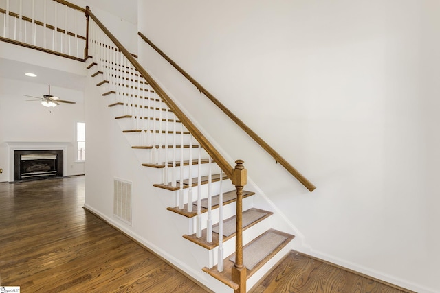 staircase with a fireplace with flush hearth, visible vents, baseboards, wood finished floors, and ceiling fan