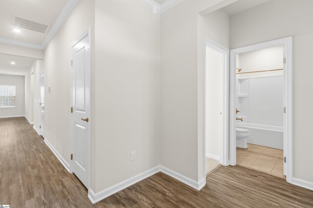 hallway featuring dark wood finished floors, visible vents, baseboards, and ornamental molding