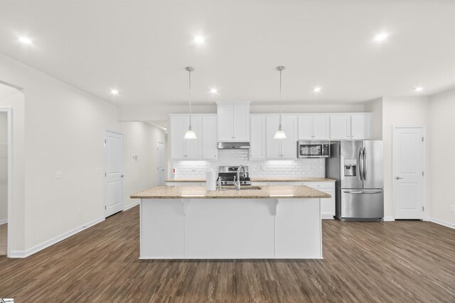kitchen with an island with sink, under cabinet range hood, stainless steel appliances, dark wood-style floors, and decorative backsplash