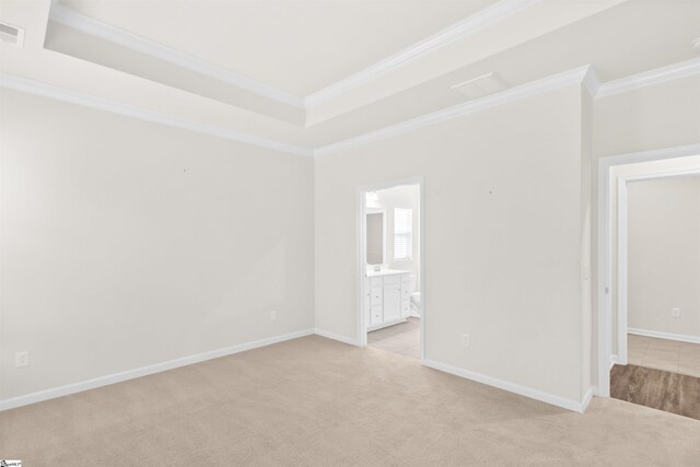 spare room featuring light carpet, a tray ceiling, visible vents, baseboards, and crown molding