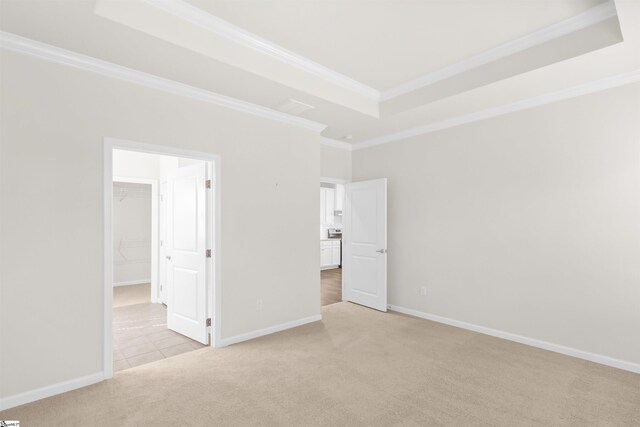 unfurnished bedroom with light carpet, a raised ceiling, baseboards, a spacious closet, and ornamental molding