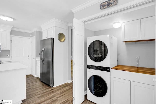 laundry room with stacked washer / drying machine, wood finished floors, ornamental molding, and laundry area