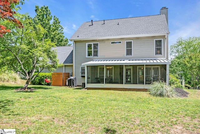rear view of property featuring a chimney, a sunroom, a yard, and roof with shingles