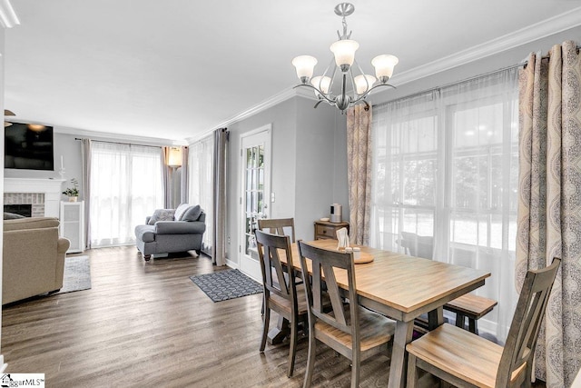 dining space featuring crown molding, wood finished floors, an inviting chandelier, a fireplace, and baseboards