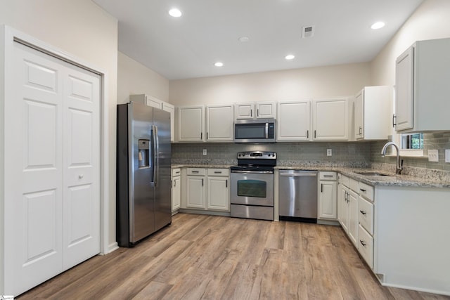 kitchen with stainless steel appliances, a sink, light stone countertops, light wood-style flooring, and tasteful backsplash