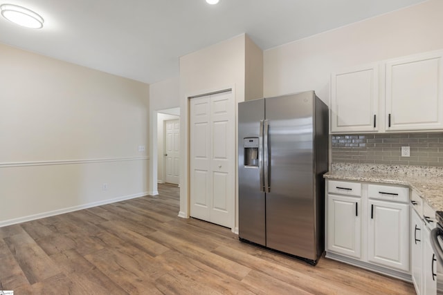 kitchen with light wood-type flooring, stainless steel fridge with ice dispenser, backsplash, white cabinetry, and light stone countertops