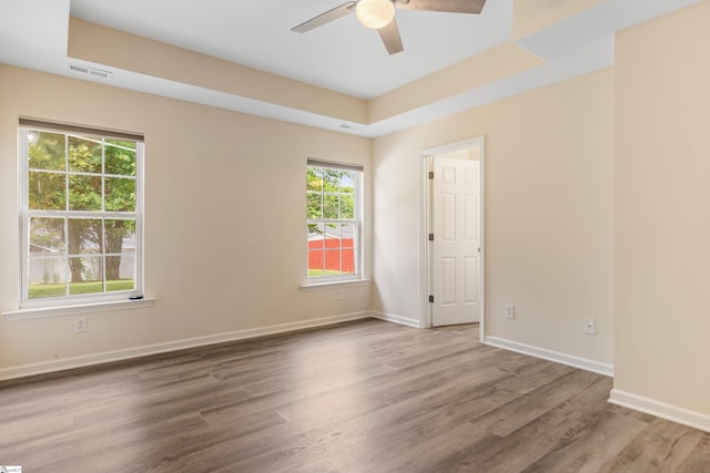 spare room featuring a tray ceiling, baseboards, visible vents, wood finished floors, and ceiling fan
