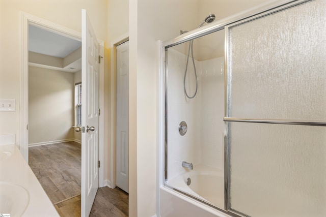 full bathroom featuring baseboards, double vanity, wood finished floors, and shower / bath combination with glass door