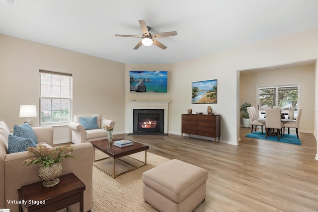 living room with a fireplace with flush hearth, baseboards, a ceiling fan, and light wood finished floors