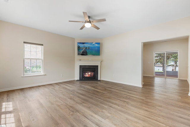 unfurnished living room with a fireplace with flush hearth, baseboards, a ceiling fan, and light wood-type flooring