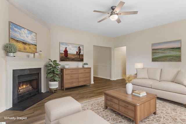 living area with a ceiling fan, a warm lit fireplace, and light wood-style floors