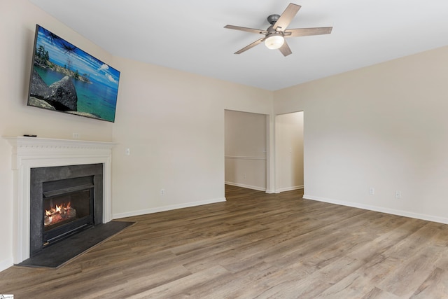 unfurnished living room with baseboards, a ceiling fan, a lit fireplace, and wood finished floors
