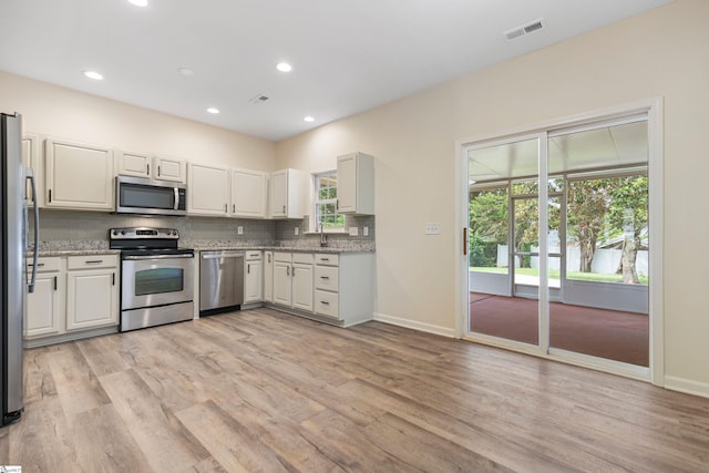 kitchen featuring light wood-style flooring, backsplash, baseboards, appliances with stainless steel finishes, and visible vents