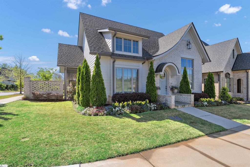 view of front of property with a shingled roof, a front lawn, and brick siding
