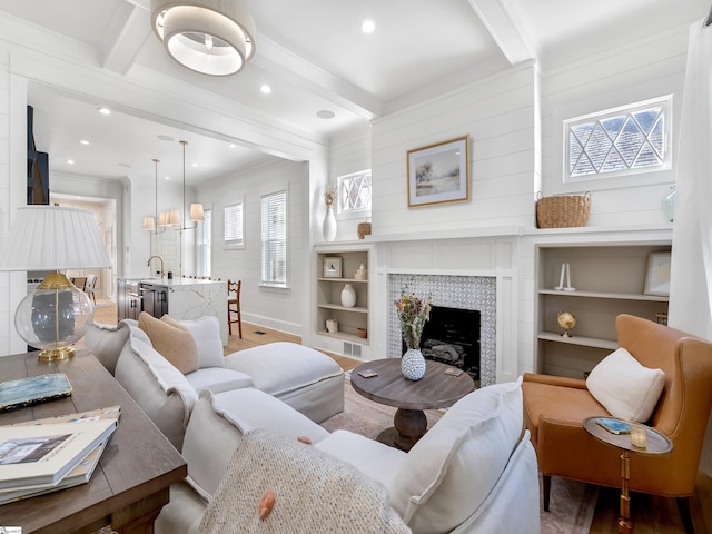 living area featuring beamed ceiling, wood finished floors, a fireplace, and ornamental molding