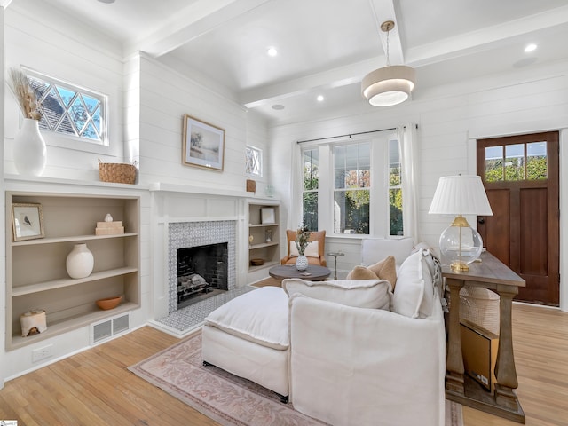 living room with built in features, a tile fireplace, beamed ceiling, light wood finished floors, and visible vents