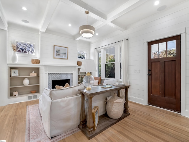 living area featuring a tile fireplace, coffered ceiling, visible vents, beamed ceiling, and light wood-style flooring