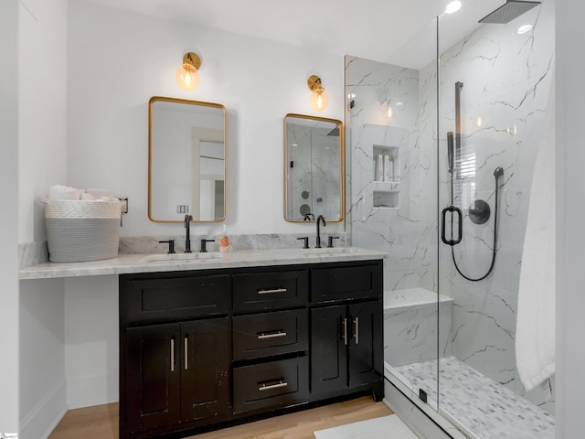 full bath with double vanity, wood finished floors, a marble finish shower, and a sink