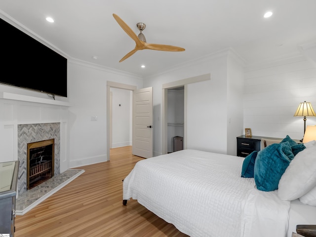 bedroom featuring light wood-style flooring, baseboards, recessed lighting, a tile fireplace, and ornamental molding