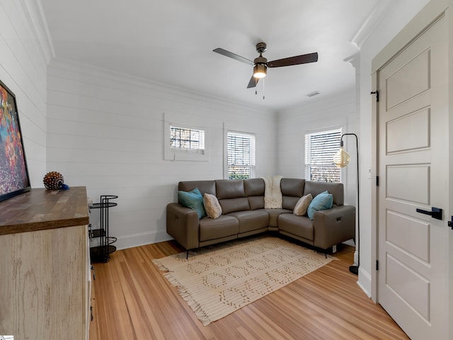 living room featuring light wood-style floors, visible vents, a ceiling fan, and crown molding