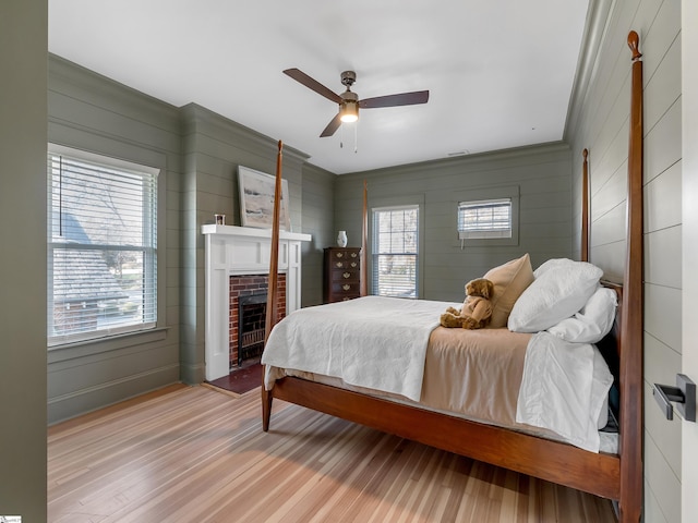 bedroom with ceiling fan, wood finished floors, wooden walls, and a fireplace