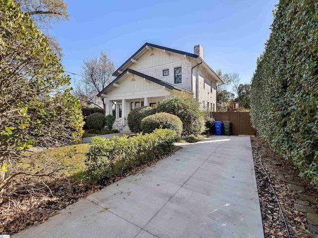 view of side of property featuring concrete driveway, a chimney, and fence